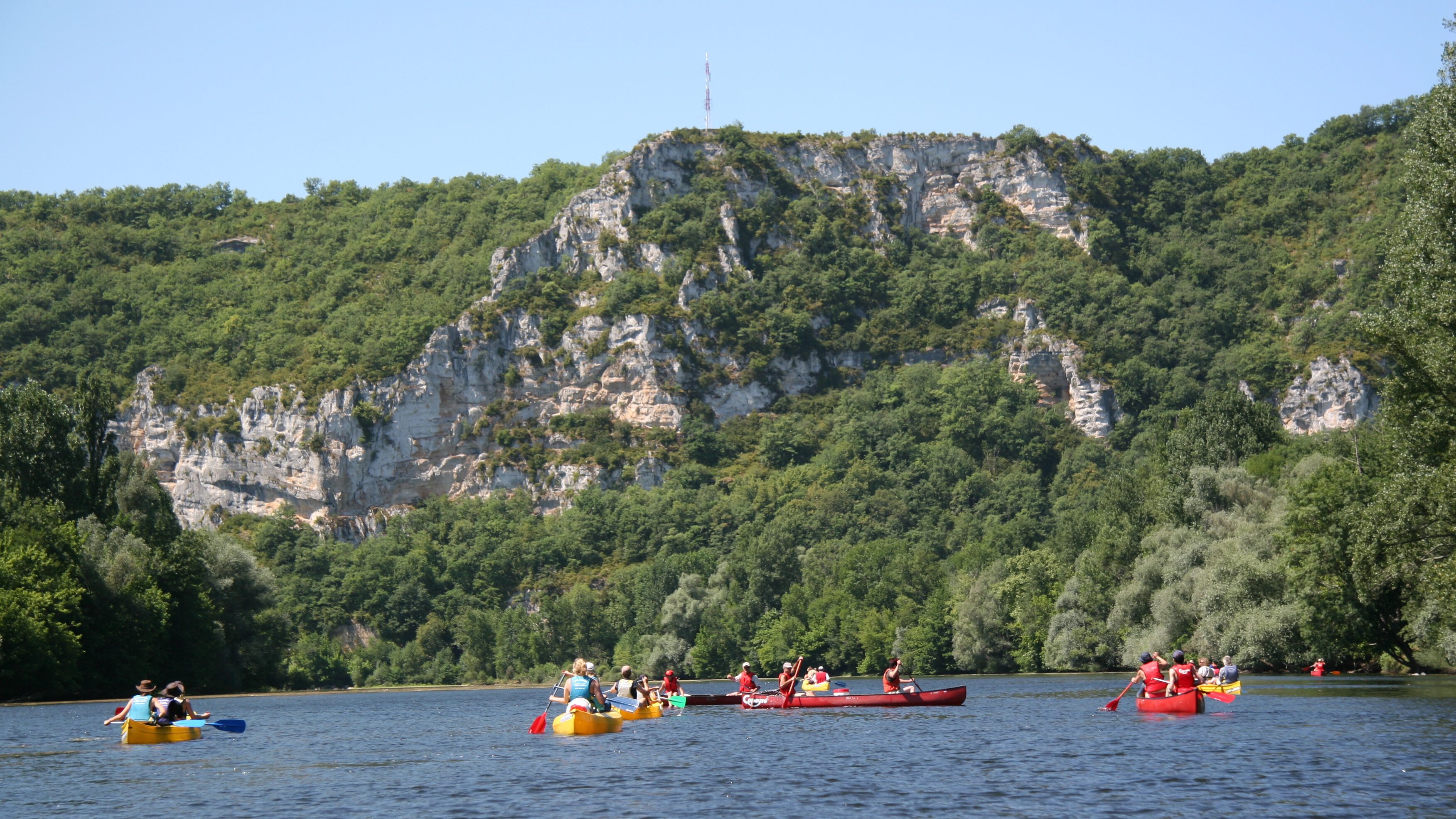 Mehrere Kanus auf der Dordogne vor einer hohen Felswand